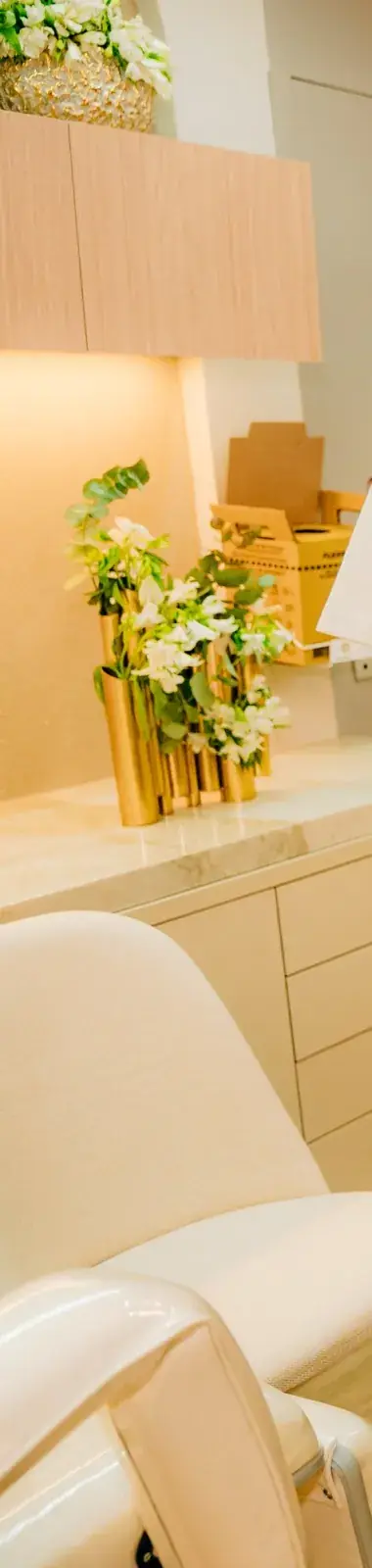 Bancada da clínica com flores brancas em vaso dourado e cadeira creme