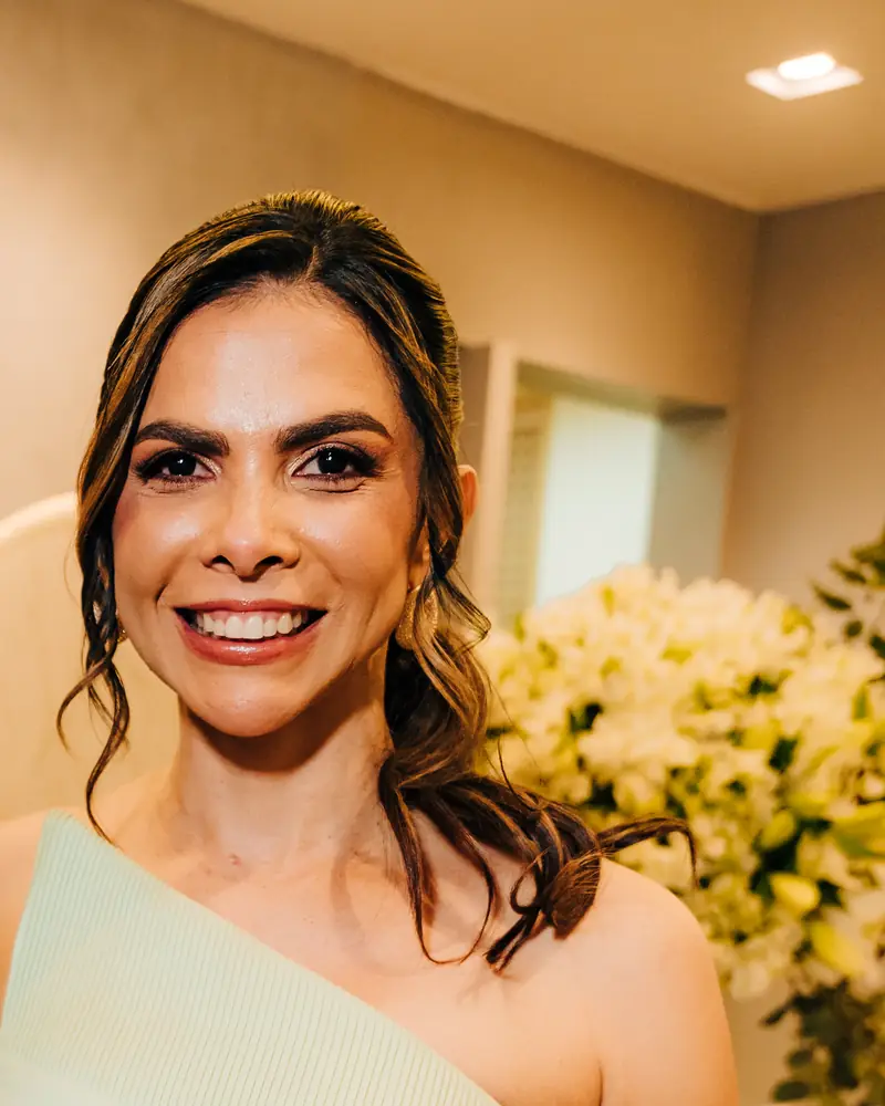 Janiele Azevedo, sorrindo, com flores brancas ao fundo