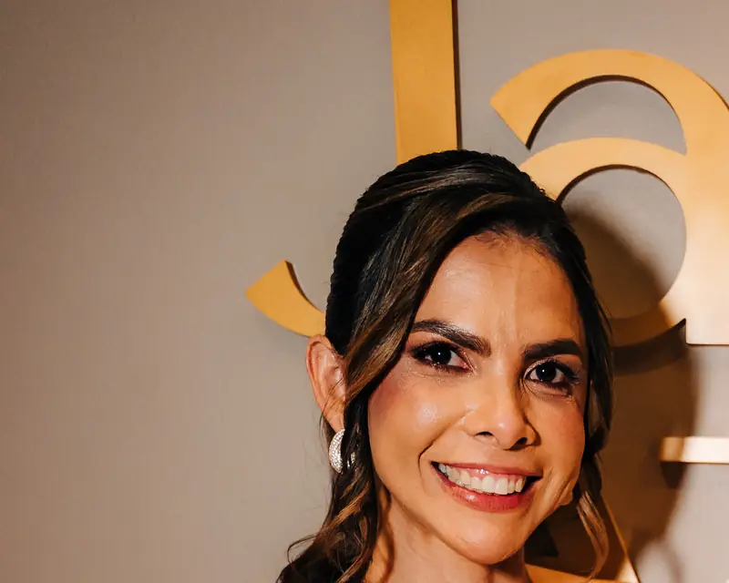 Janiele Azevedo, sorrindo, diante das letras douradas da clínica